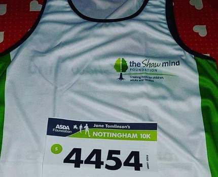 A photo of a white vest with green colour accents, the numbers 4454 on a running bib, a runner preparing for a marathon
