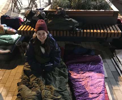 Photo of a woman sitting on the ground with a winter jacket on and a sleeping bag