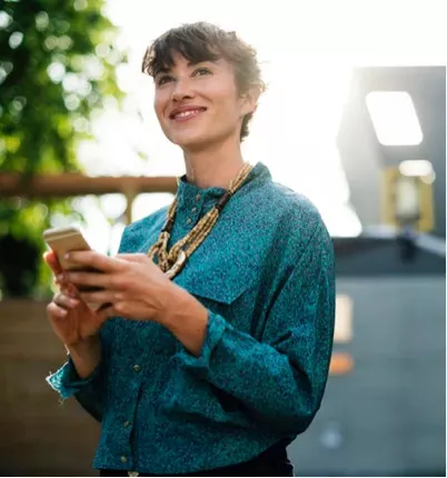 A woman in a blue shirt looking up from her phone screen.